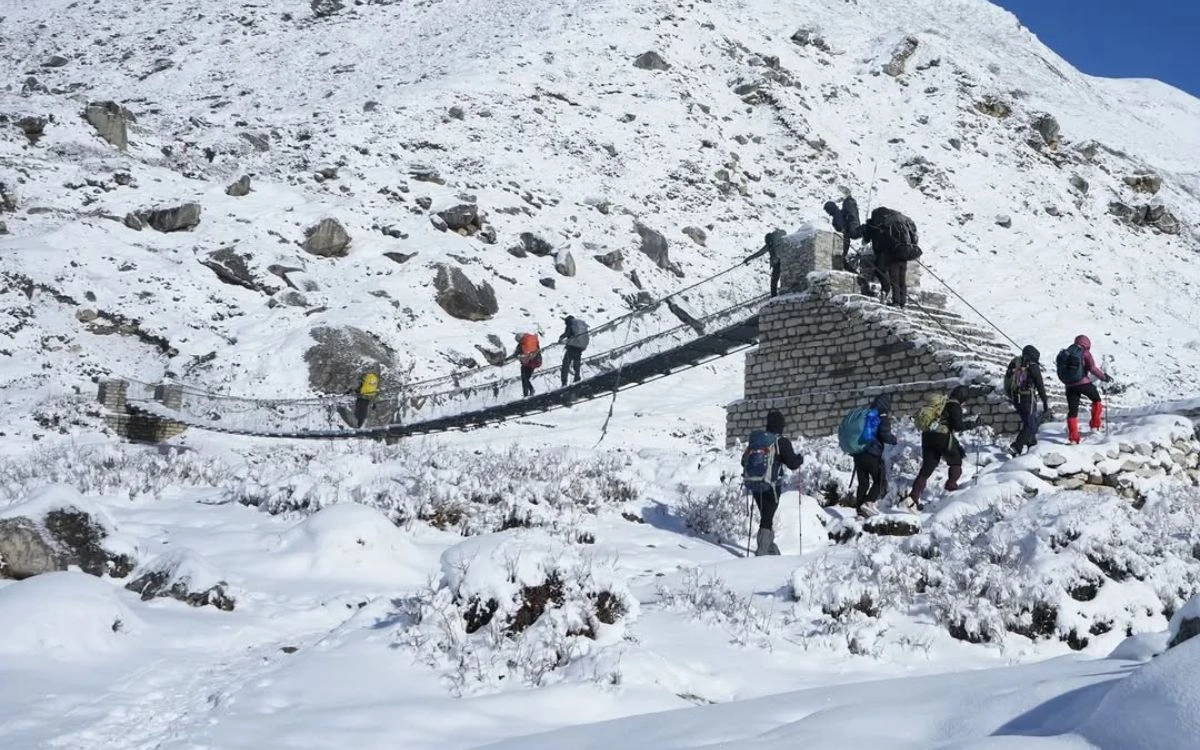 A group of trekkers crossing a suspension bridge over a snow-blanketed Himalayan landscape in Nepal