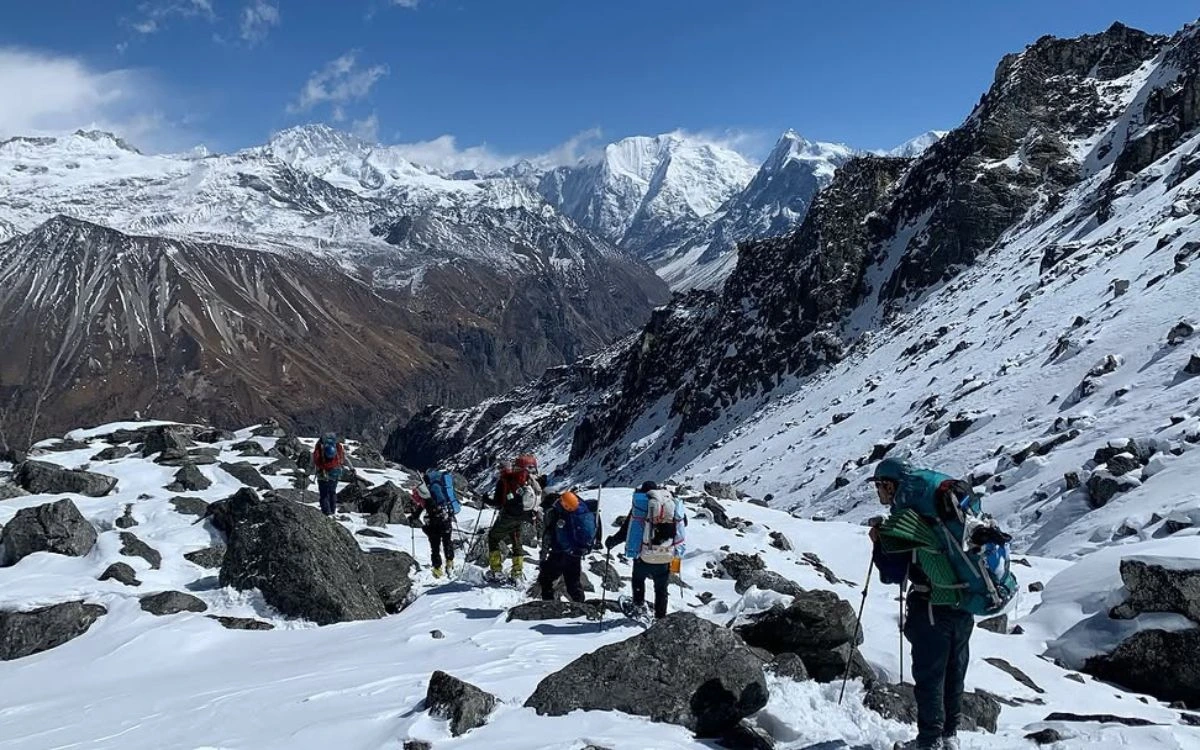 Trekking group ascending rocky snow-covered Ganjala Pass with Himalayan peaks behind