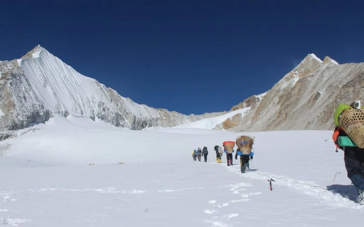 Expedition team with heavy loads crossing pristine snowfield between steep mountain walls