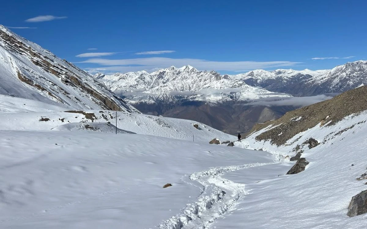 Lone trekker descending snowy Thorong La Pass with Annapurna range panorama