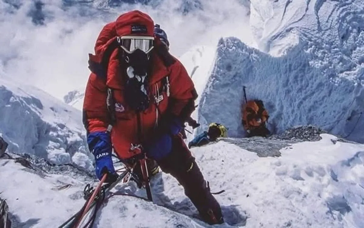 Climber in red jacket on Hillary Step with panoramic view of Himalayan peaks and clouds below
