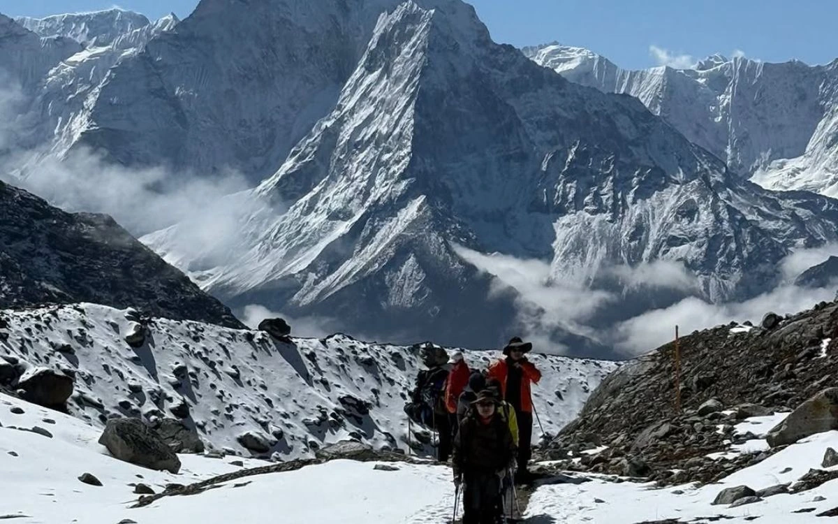 Trekkers following licensed guide through high-altitude Himalayan trail with dramatic mountain peaks and clouds
