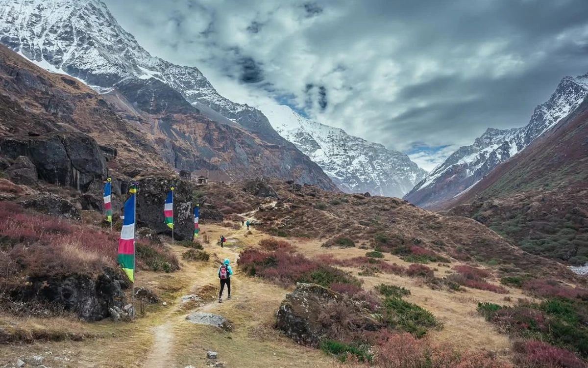Solo trekker walking a mountain trail past Buddhist prayer flags in Nepal