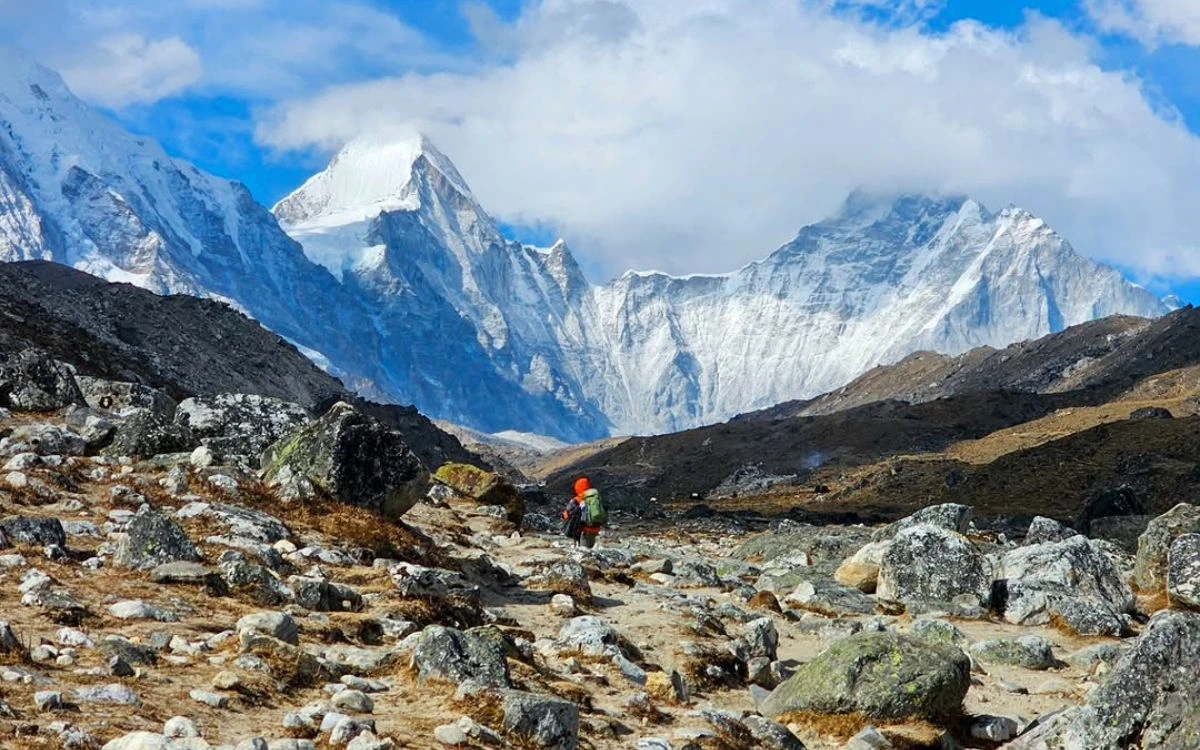 Hiker with a large backpack on a rocky trail towards snow-capped Himalayan peaks