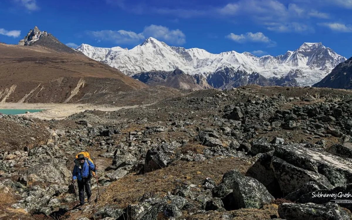 Trekker with backpack hiking rocky terrain with snow-capped Himalayan peaks in background