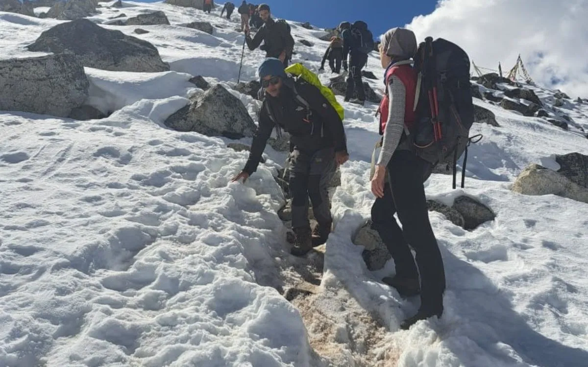 Group of trekkers navigating snowy mountain terrain with hiking poles.
