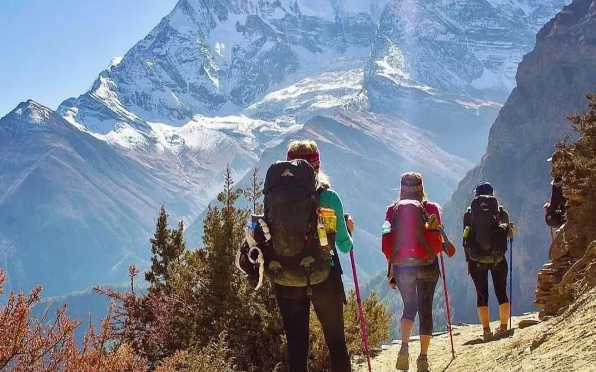 Trekkers with backpacks walking on a mountain trail with dramatic Himalayan peaks behind them.
