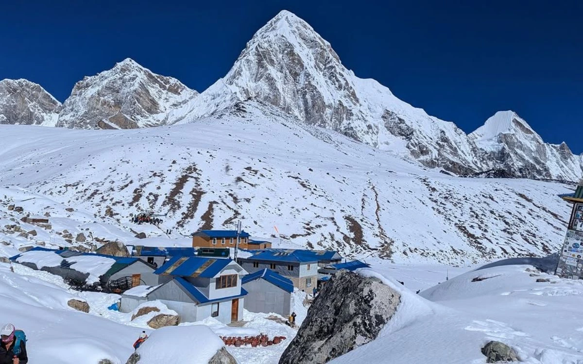 Snow-covered mountain lodges with blue roofs beneath towering Himalayan peaks