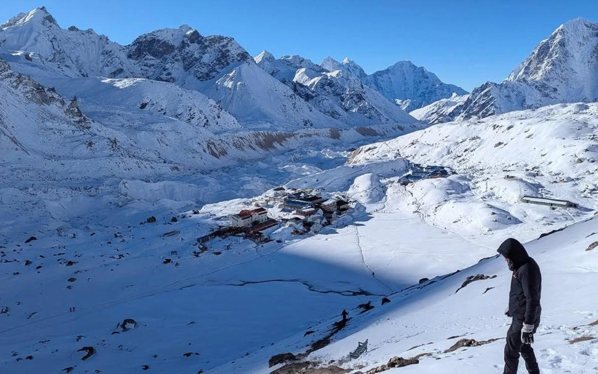 Solo trekker overlooking snow-covered mountain village in winter valley