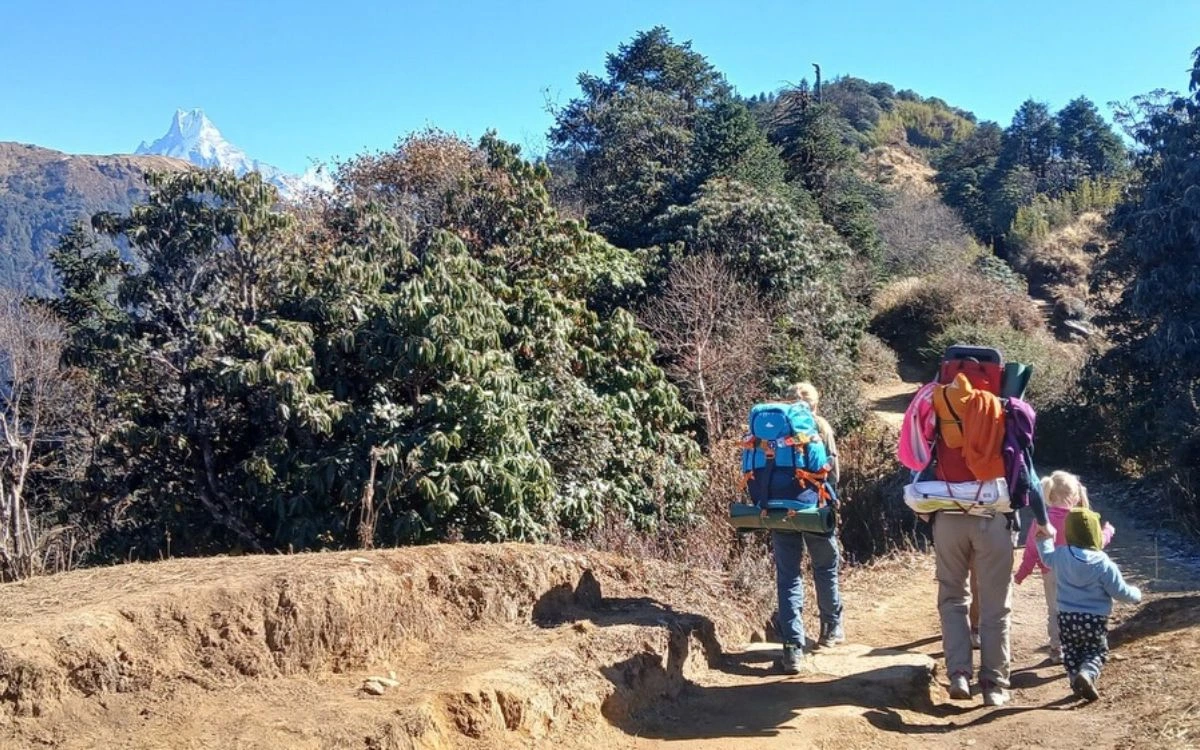Family with young child trekking on mountain trail with snow peak in distance