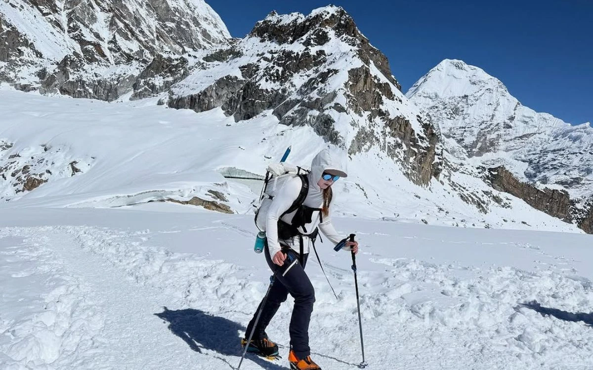 Female climber ascending snowy slope with rocky mountain face behind
