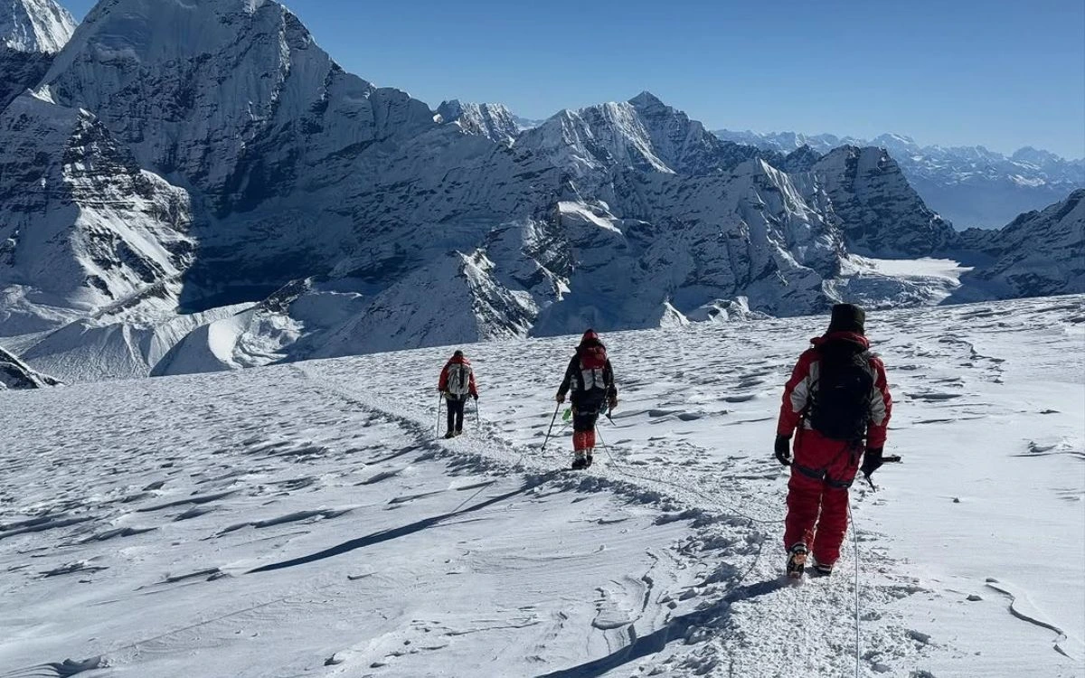 Three climbers trekking across wide snow field toward distant Mera peak