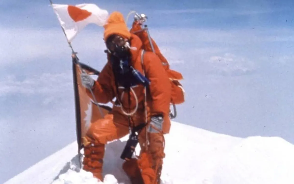 Junko Tabei at Everest summit in orange mountaineering suit holding Japanese flag