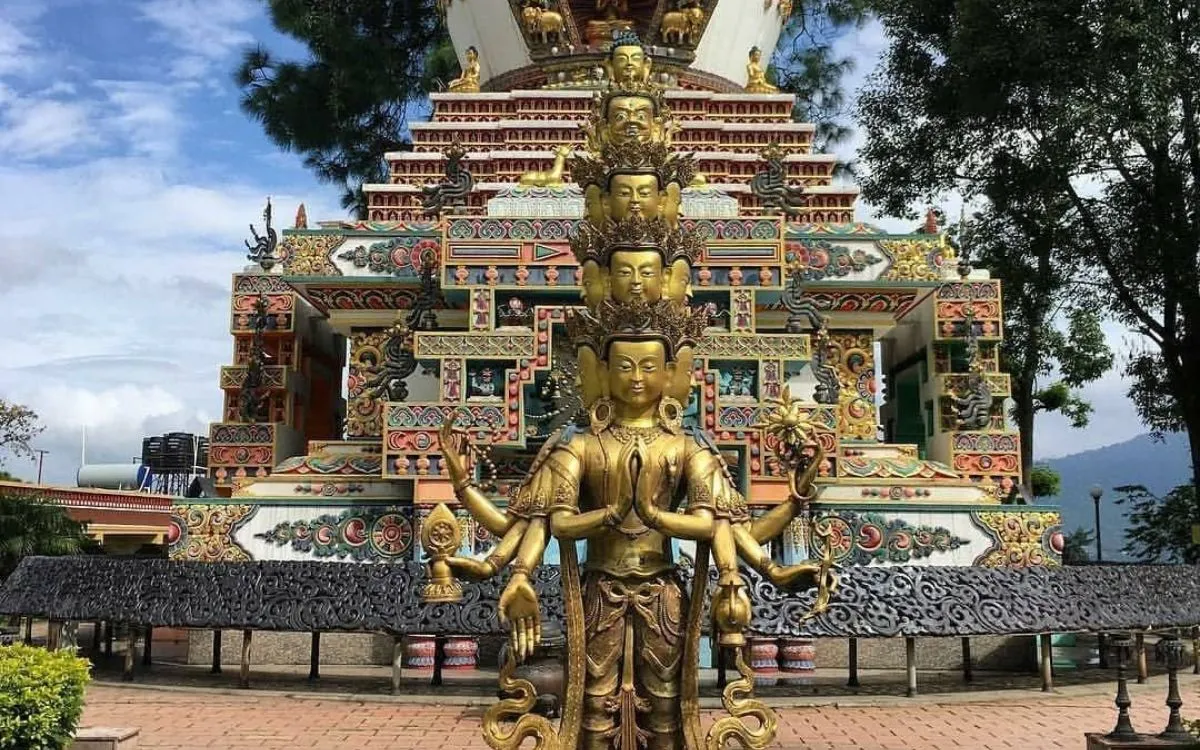 Golden multi-armed Avalokitesvara (Chenrezig) statue with multiple heads standing in front of the ornately decorated stupa at Kapan Monastery