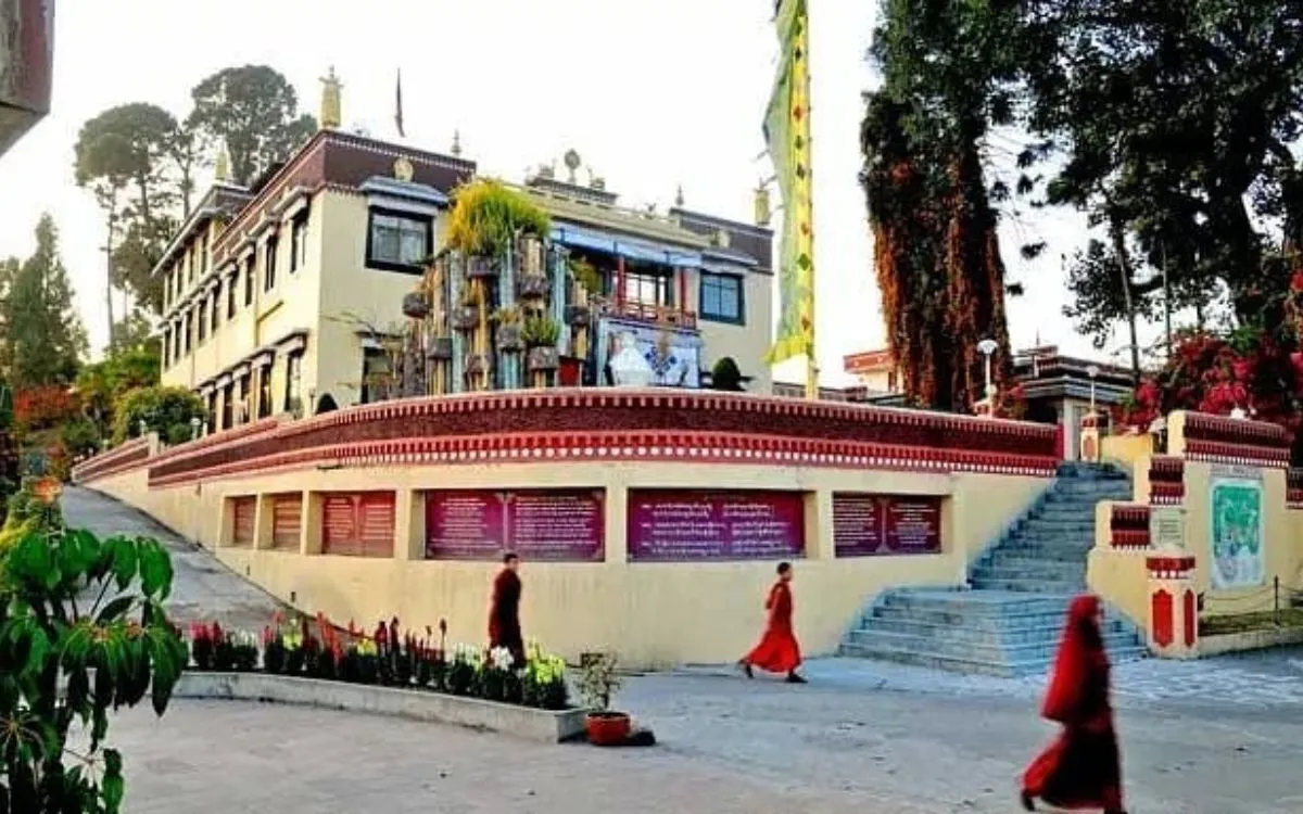 Buddhist monks in traditional red robes walking past the Tibetan-style buildings and prayer inscription walls of Kapan Monastery, Kathmandu, Nepal
