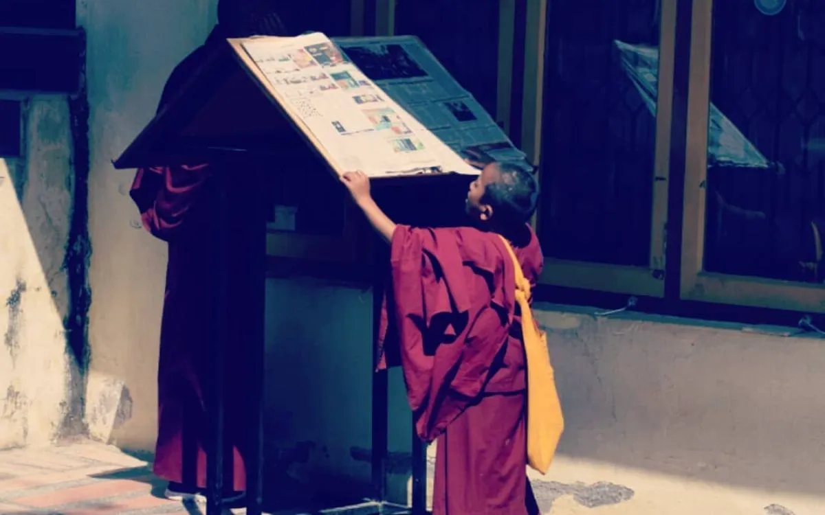 Young novice monk in red and yellow robes reading a notice board outside Kapan Monastery