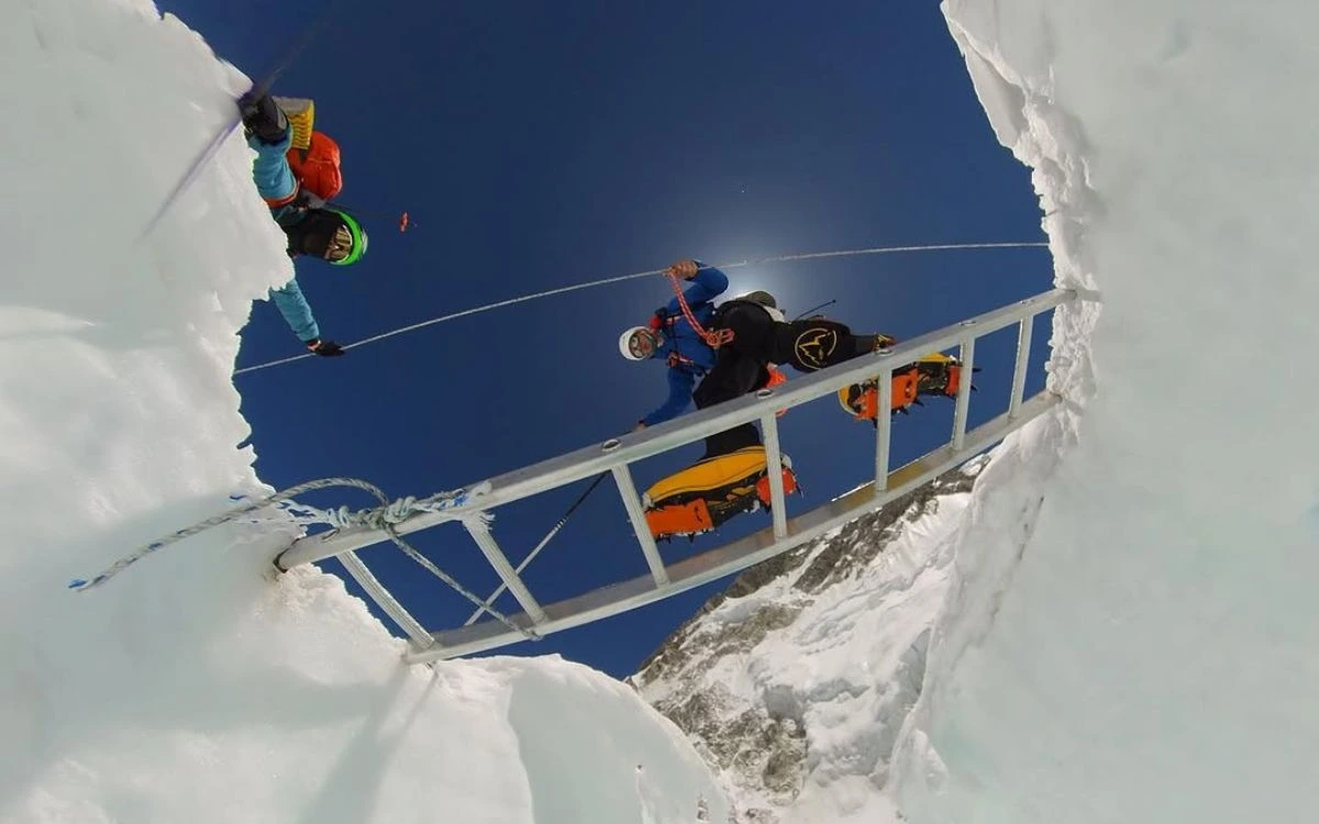 Climbers crossing a horizontal ladder over a deep crevasse in the Khumbu Icefall