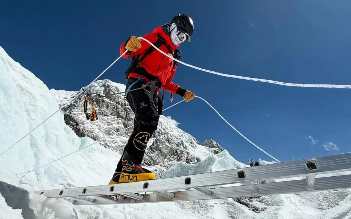 Climber in crampons crossing an aluminum ladder over a Khumbu Icefall crevasse