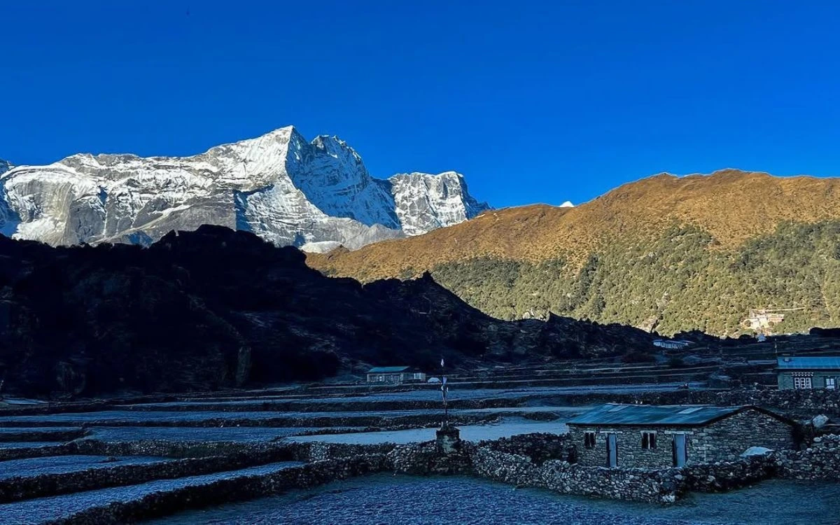 Stone-walled fields of Khumjung village at dusk with snow-capped Himalayan peaks rising against a deep blue sky