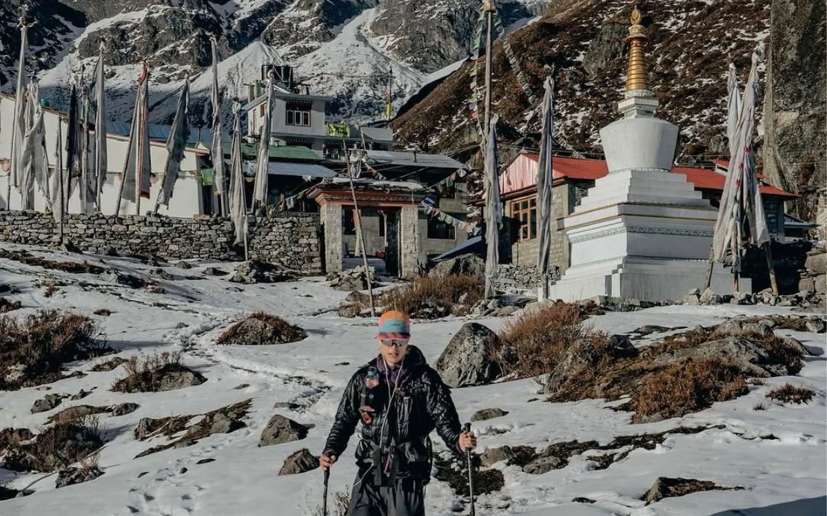 Trekker with hiking poles at Kyanjin Gompa Buddhist stupa in snowy Langtang Valley