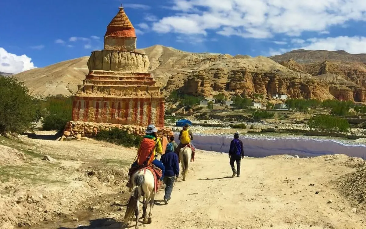 Trekkers on horseback approaching ornate Buddhist chorten in Upper Mustang's arid terrain
