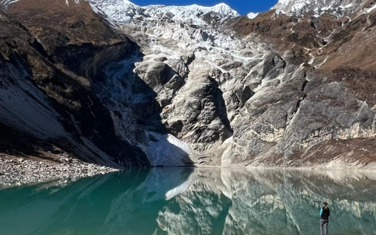 Glacial lake with emerald waters reflecting rocky cliffs and glacier along Manaslu Circuit hiking trail in Nepal Himalayas