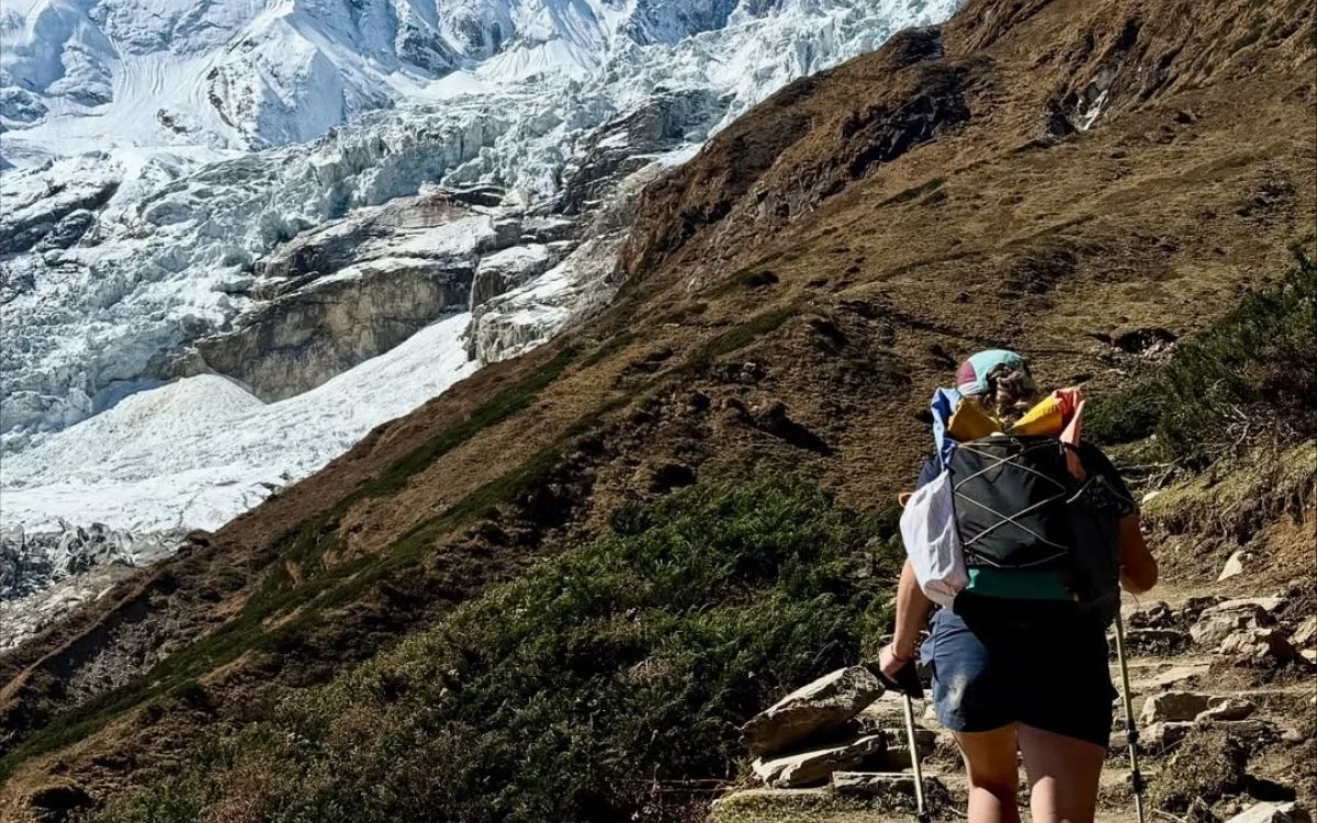 Solo trekker with backpack hiking steep trail with massive glacier and ice formations visible on Manaslu Circuit Nepal