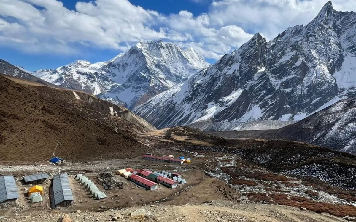Mountain lodge accommodation and camping tents at high altitude base with dramatic snow-capped Himalayan peaks on Manaslu Circuit