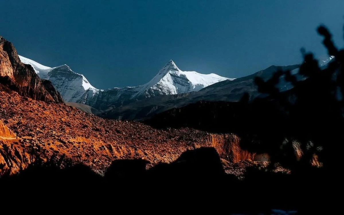 Dramatic dusk view of sharp snow-capped peaks above rust-red rocky slopes in the Manang Valley