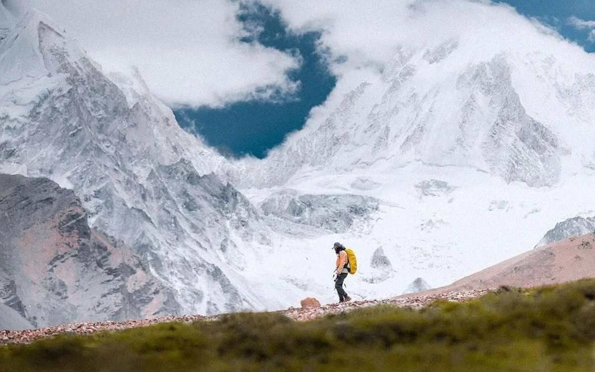 Lone trekker with a yellow pack walking a high ridge dwarfed by towering snow and glacier walls near Manang