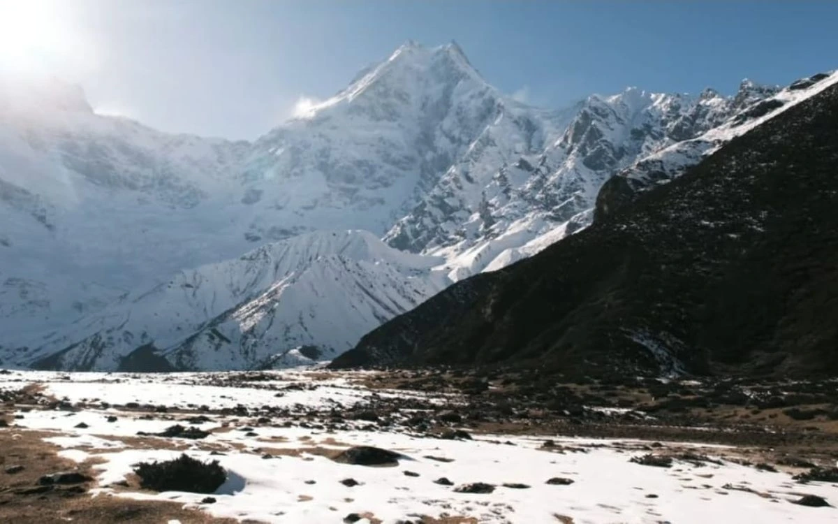 Snow-covered alpine meadow below dramatic Himalayan mountain peaks