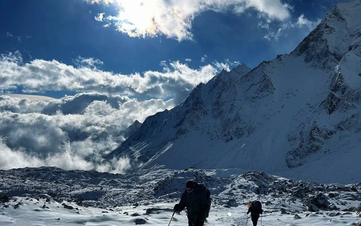 Trekkers crossing snowy terrain with dramatic mountain backdrop and clouds