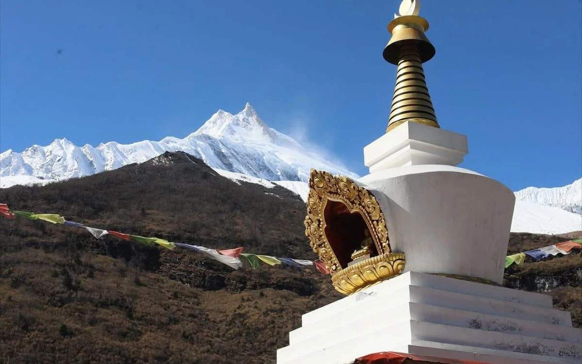 White Buddhist stupa with golden ornaments and prayer flags, Mount Manaslu in background