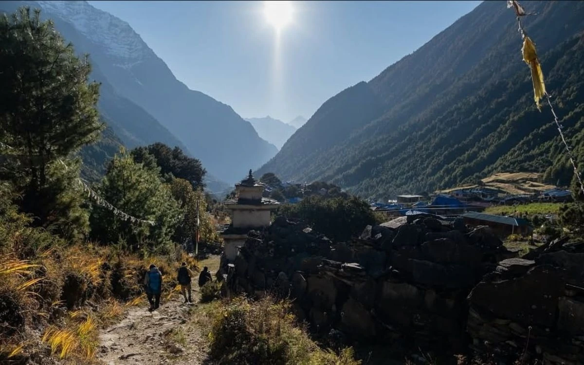 Buddhist chorten and prayer flags on mountain trail with village in background
