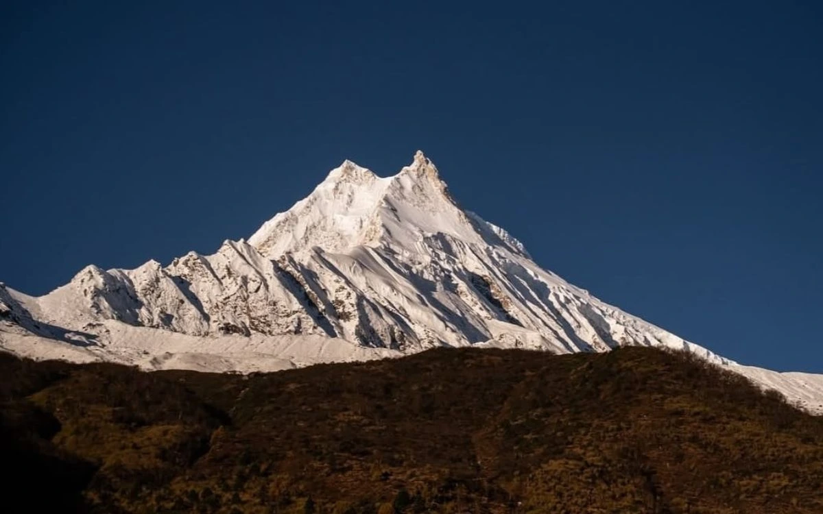 ount Manaslu peak rising above alpine meadows against blue sky