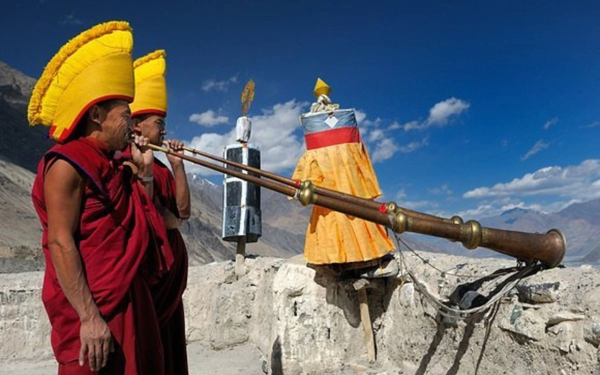 Two Buddhist monks in ceremonial robes playing traditional horns during the Tiji festival