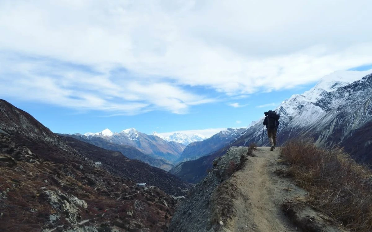Trekker on mountain trail with snow-capped Himalayan peaks under clear blue sky