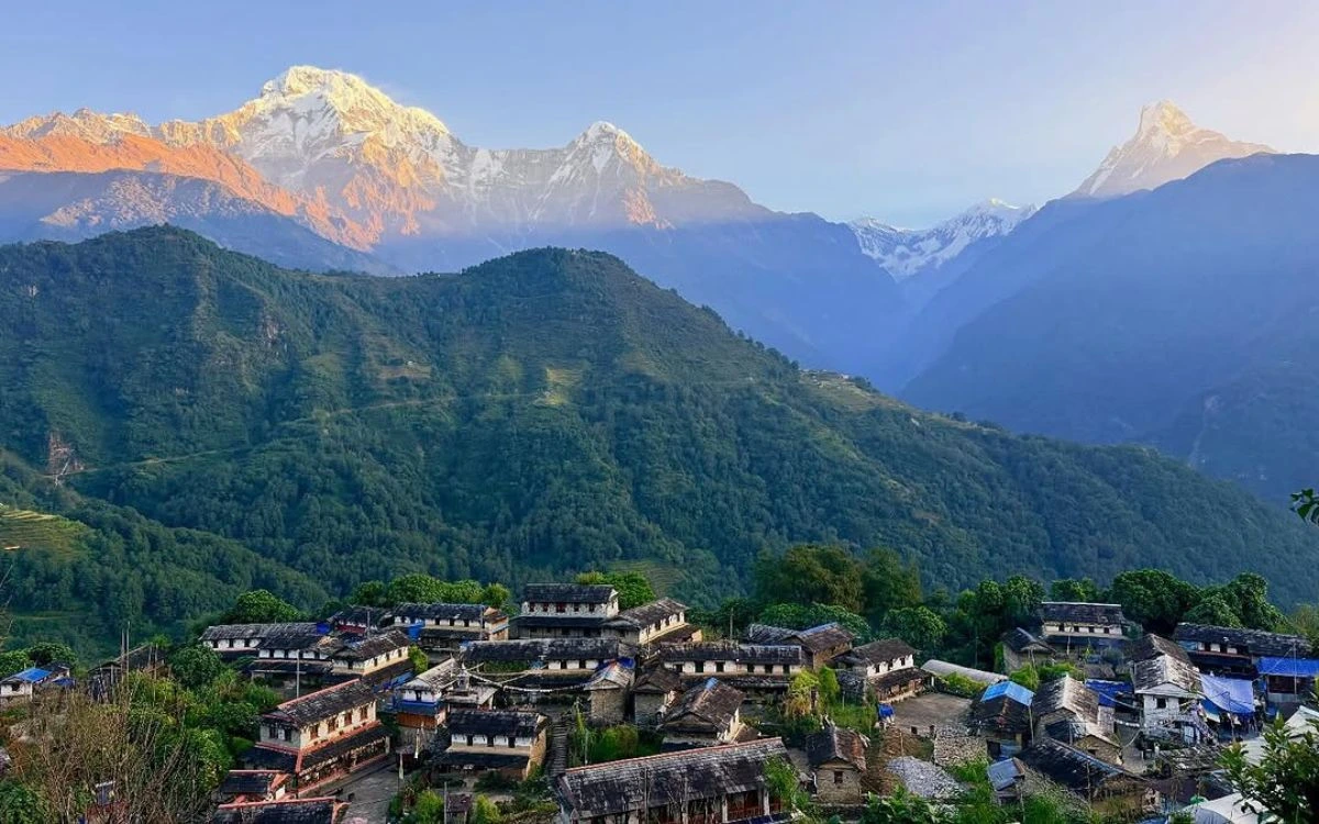 Traditional Nepali village with stone houses beneath Annapurna mountain range at dawn