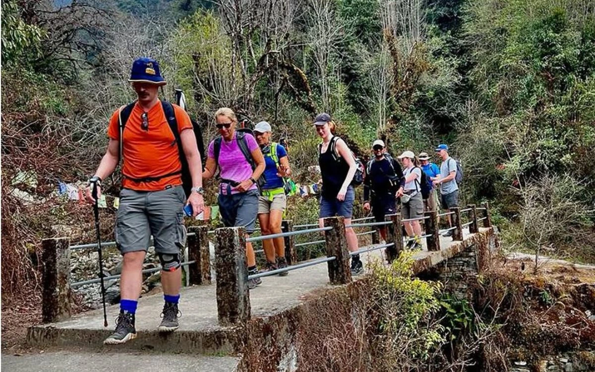 Group of trekkers crossing a stone bridge through a forest trail in Nepal