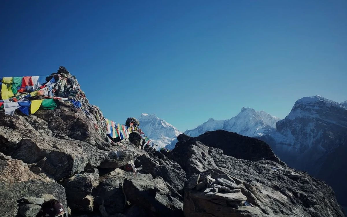 Colorful prayer flags on a rocky summit with snow-capped Himalayan peaks behind