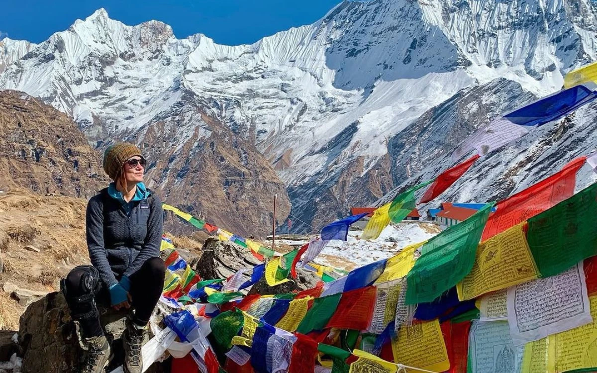 Solo trekker sitting beside colorful prayer flags with Annapurna range behind