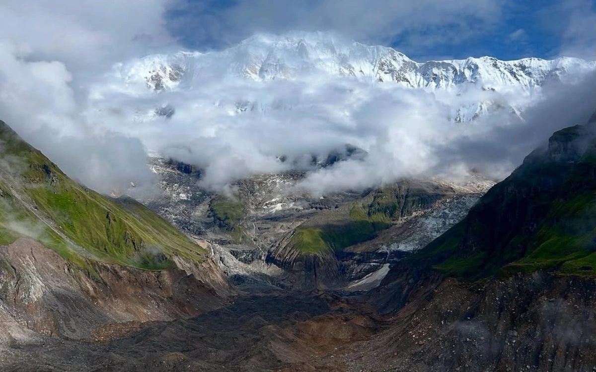 Snow-capped Himalayan peak partially wrapped in monsoon clouds above a glacial valley