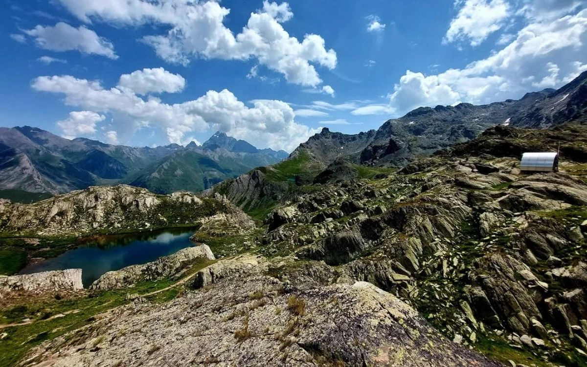 Rocky high-altitude terrain with a small mountain lake and jagged peaks under a summer sky