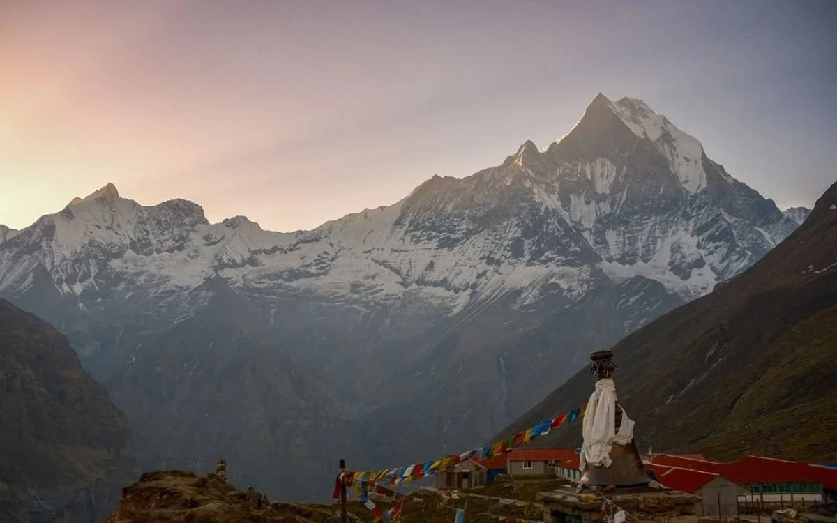 Machhapuchhre peak glowing at dusk above Annapurna Base Camp teahouses with colorful prayer flags