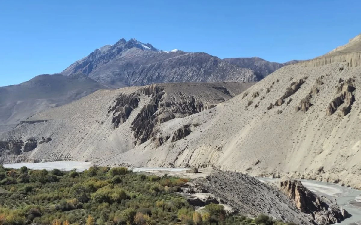 The dry arid Mustang valley with a braided river, eroded cliffs, and a rocky peak under a clear blue sky