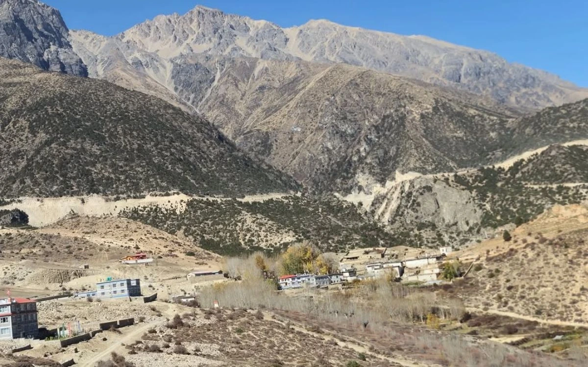 A small Mustang village with autumn trees nestled in a dry barren valley beneath a massive rocky ridge