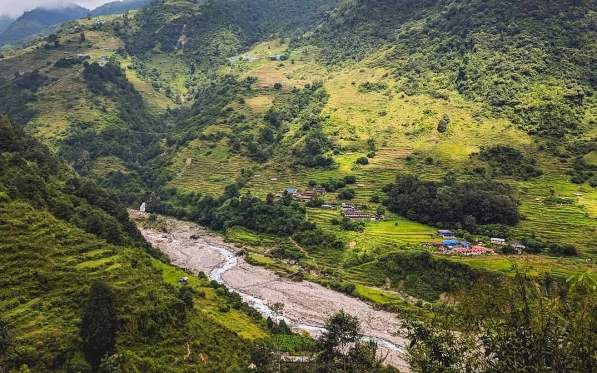 Lush green terraced hillsides and a river valley with a small Nepali village