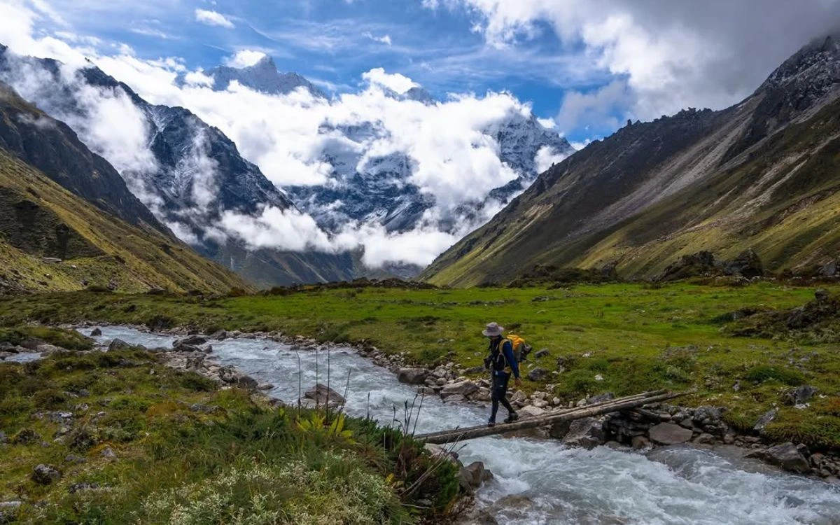 Trekker crossing a log bridge over a mountain stream in Nepal