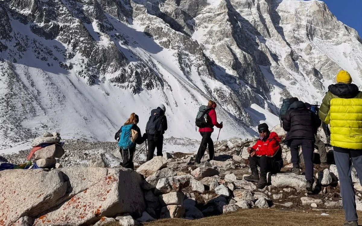 A group of trekkers resting on large boulders below a dramatic snow-covered Himalayan peak in Nepal
