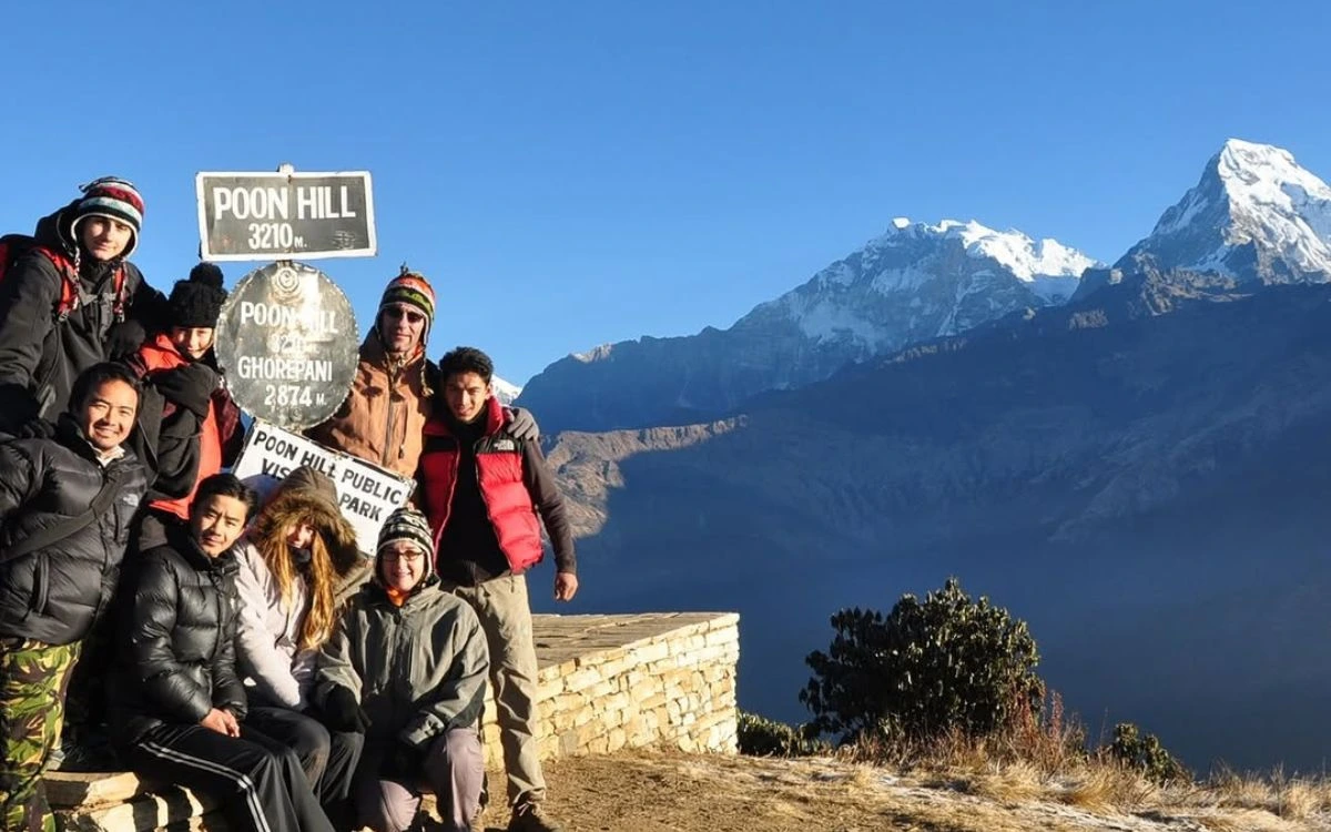 Group of trekkers posing at Poon Hill summit sign at 3,210m with Annapurna views